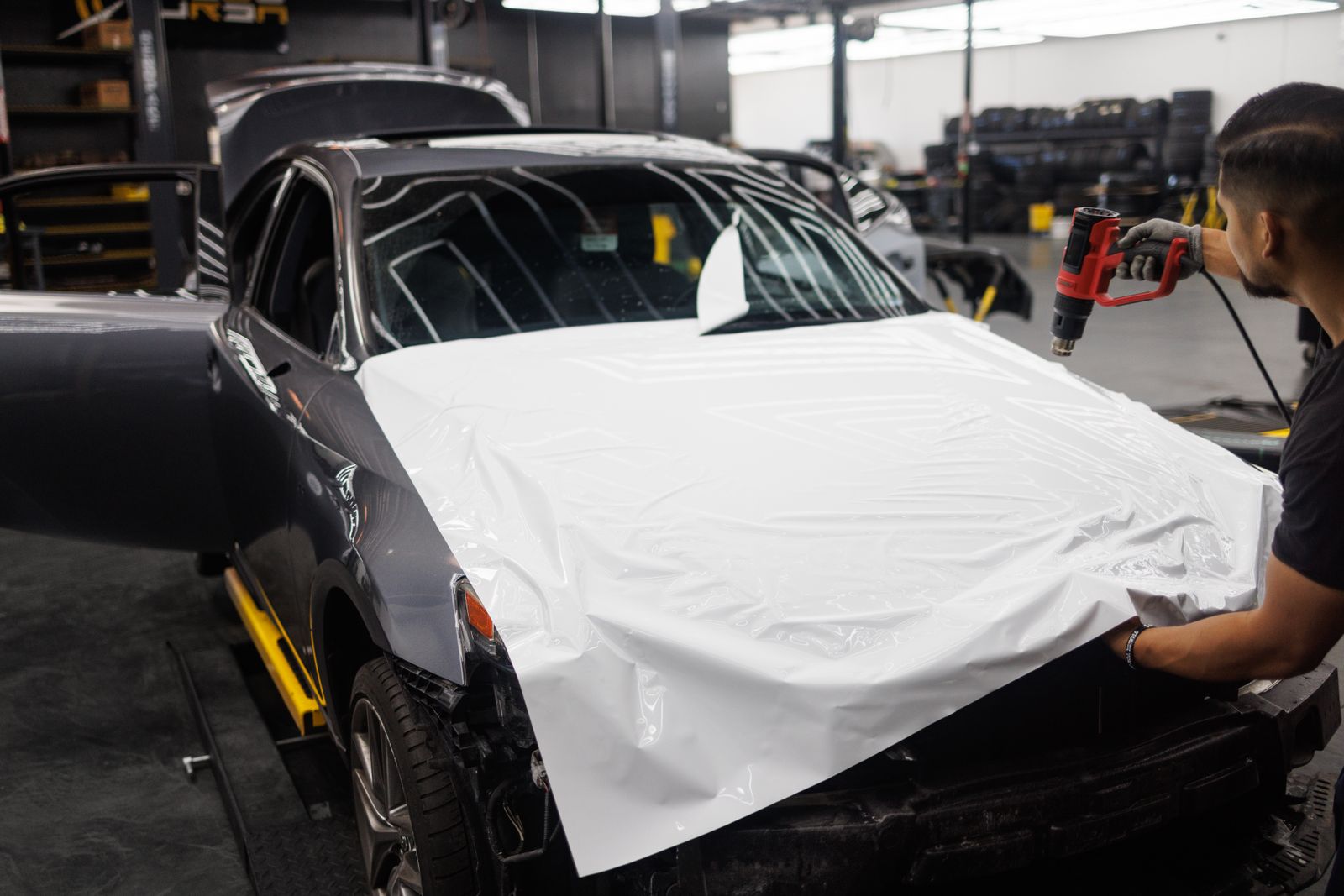 Installer smoothing protective film onto a car panel in the bay